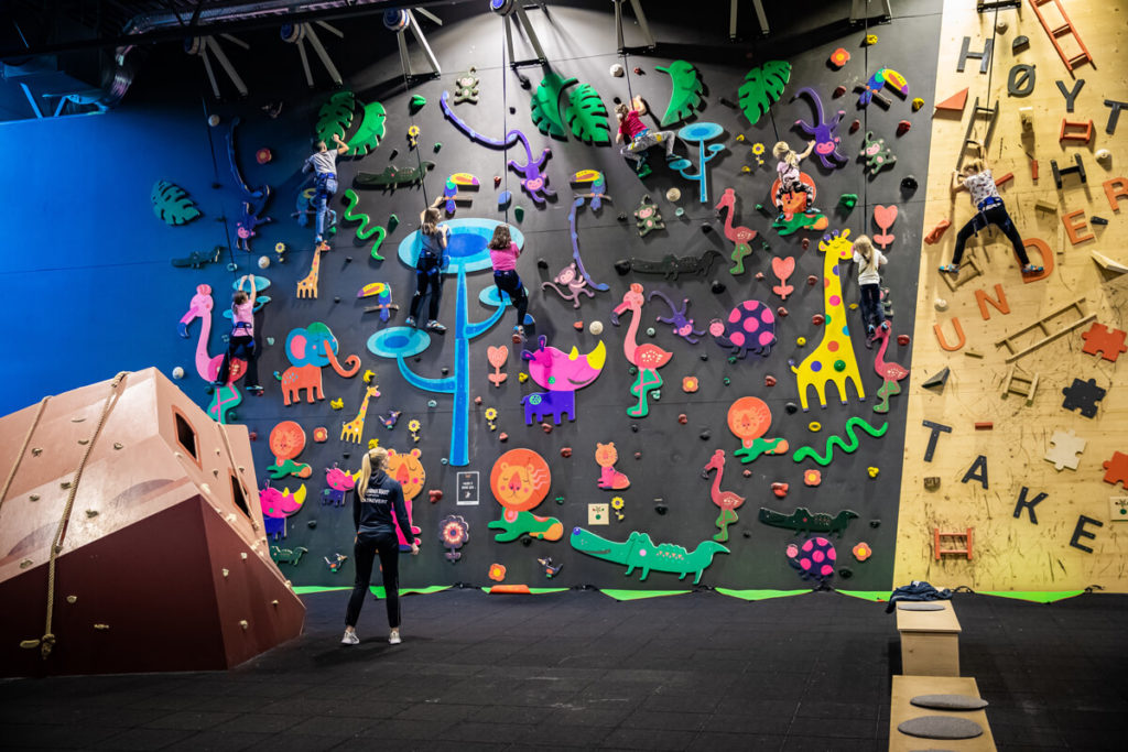 Barn og voksne som klatrer på fargerik temaklatrevegg med dyremotiver hos Høyt Under Taket