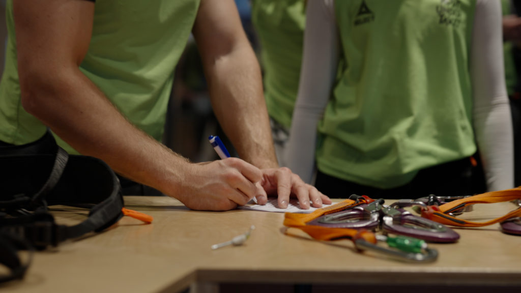 Ansatt registrerer deltakere under teambuilding i klatresenter med klatreutstyr på bordet