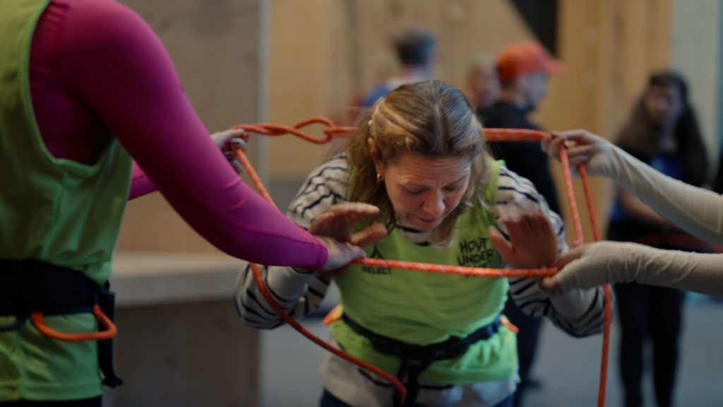 Ansatte i teambuilding-øvelse samarbeider med tauaktivitet i klatrehall hos Høyt Under Taket