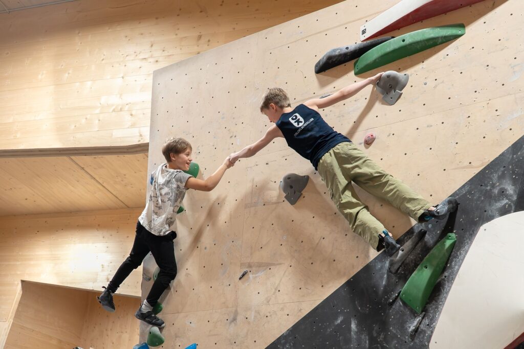 To barn klatrer på innendørs klatrevegg og hjelper hverandre hos Høyt Under Taket