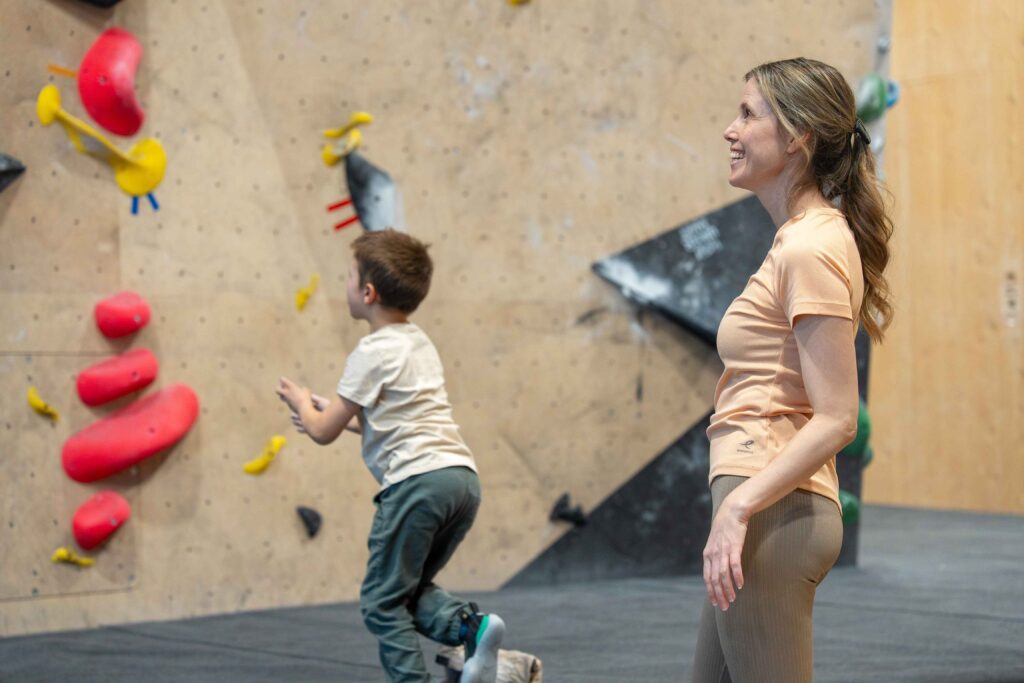 Barn klatrer på innendørs klatrevegg mens voksen følger med hos Høyt Under Taket